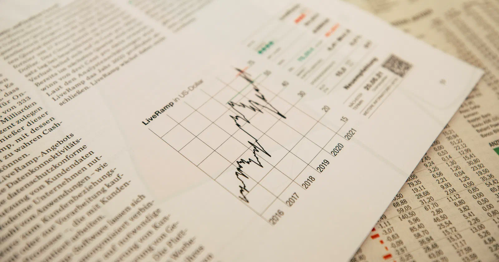 A printed financial page with figures and charts held above a laptop keyboard